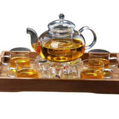Glazen theepot met zes kopjes op houten dienblad, gevuld met warme thee, voor gezellige theemomenten.