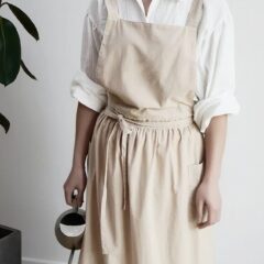 Persoon in beige schort met gieter, klaar om planten water te geven. Minimalistisch interieur.