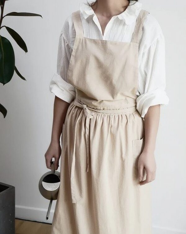 Persoon in beige schort met gieter, klaar om planten water te geven. Minimalistisch interieur.