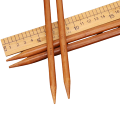 Bamboe breinaalden en houten liniaal op zwarte achtergrond voor handwerk en naaiprojecten.