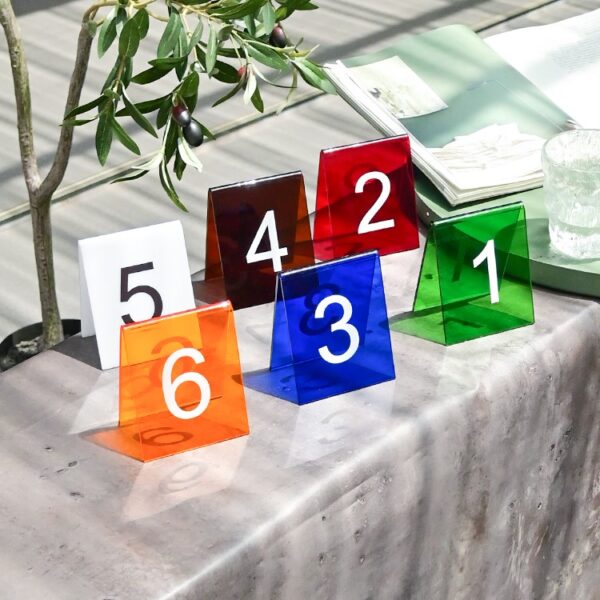 Gekleurde tafelnummers van 1 tot 6 op een tafel naast een plant en een open boek.