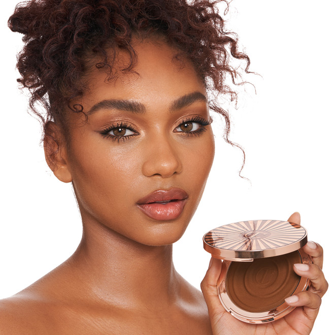 Vrouw toont luxe bronzer in stijlvolle verpakking voor een natuurlijke gloed. Perfect voor elke make-up liefhebber.