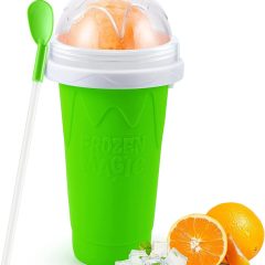 Groene Frozen Magic-beker met lepel, gevuld met sinaasappelsorbetijs en ijsklontjes. Perfect voor zomerse verfrissing.