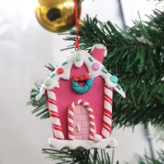 Kerstversiering: roze peperkoekhuisje met snoeppatronen, hangend in kerstboom. Charmant en feestelijk decor.