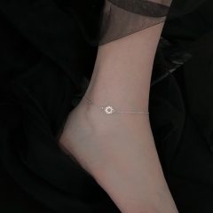 Enkel met elegante zilveren enkelband en zon bedel tegen zwarte achtergrond. Perfect voor modieuze sieradenstijl.