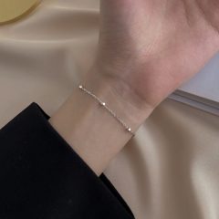 Minimalistische zilveren armband met fijne schakels om de pols, gedragen op een zijden achtergrond.