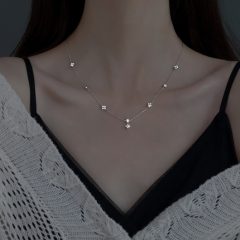 Vrouw draagt stijlvolle, delicate zilveren ketting met bloemaccenten over schouderbedekkend wit kant en zwarte top.