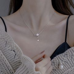 Vrouw draagt een elegante zilveren ketting met bloemhanger, gecombineerd met een gebreide trui voor een stijlvolle look.