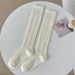 Witte kabelgebreide kniekousen op een witte tafel naast een open tijdschrift en een kaars.