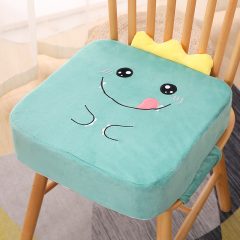 Groen kussen met schattig cartoongezicht op houten stoel, ideaal voor kinderkamer of speelse woondecoratie.